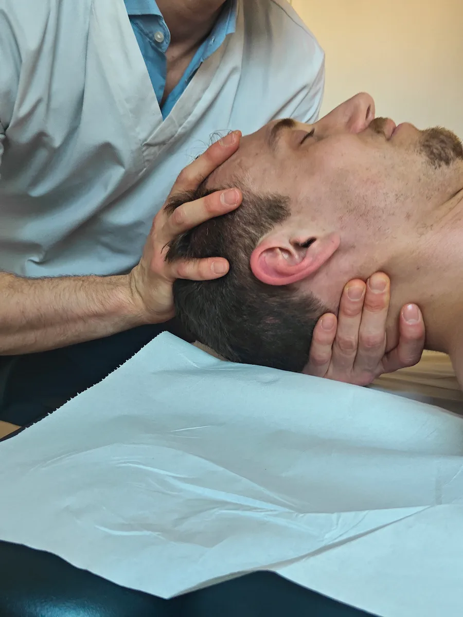 Ostéopathe réalisant un travail doux de la base du crâne et des cervicales chez un patient allongé.